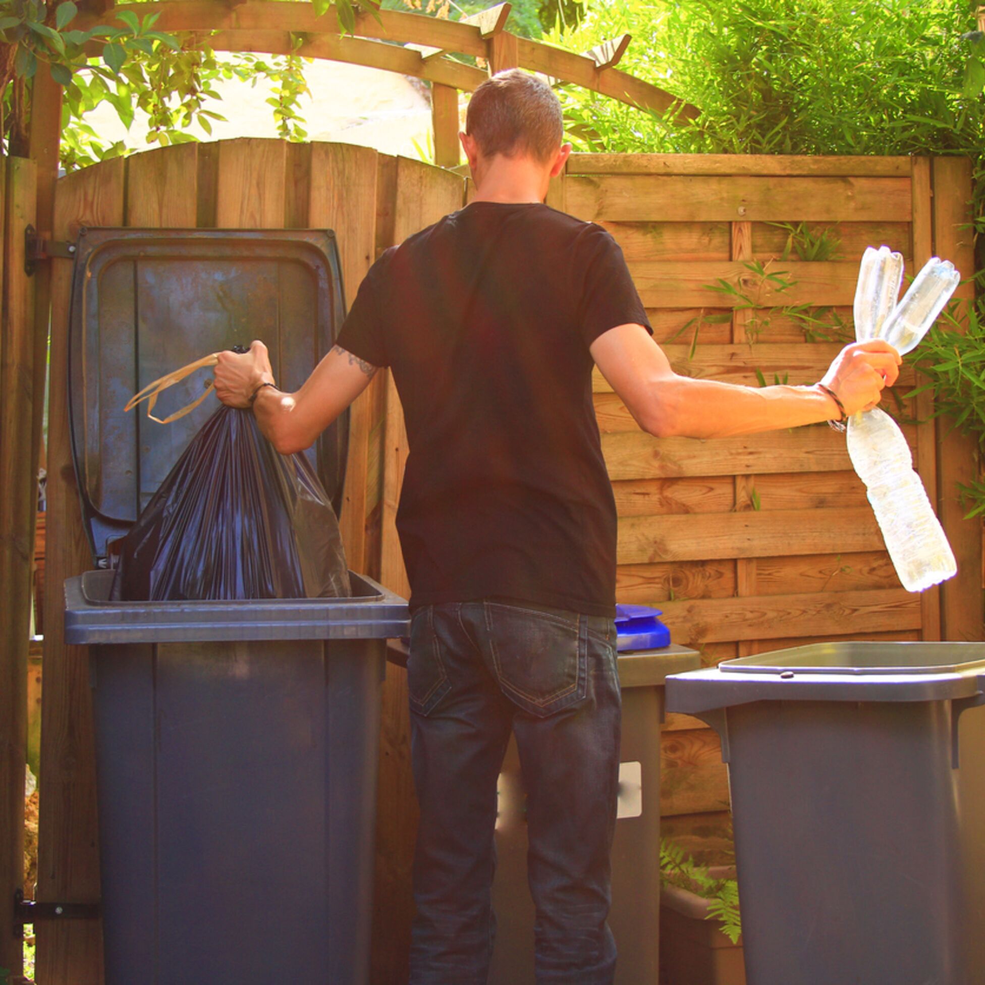 Mann sortiert Müll in Tonnen