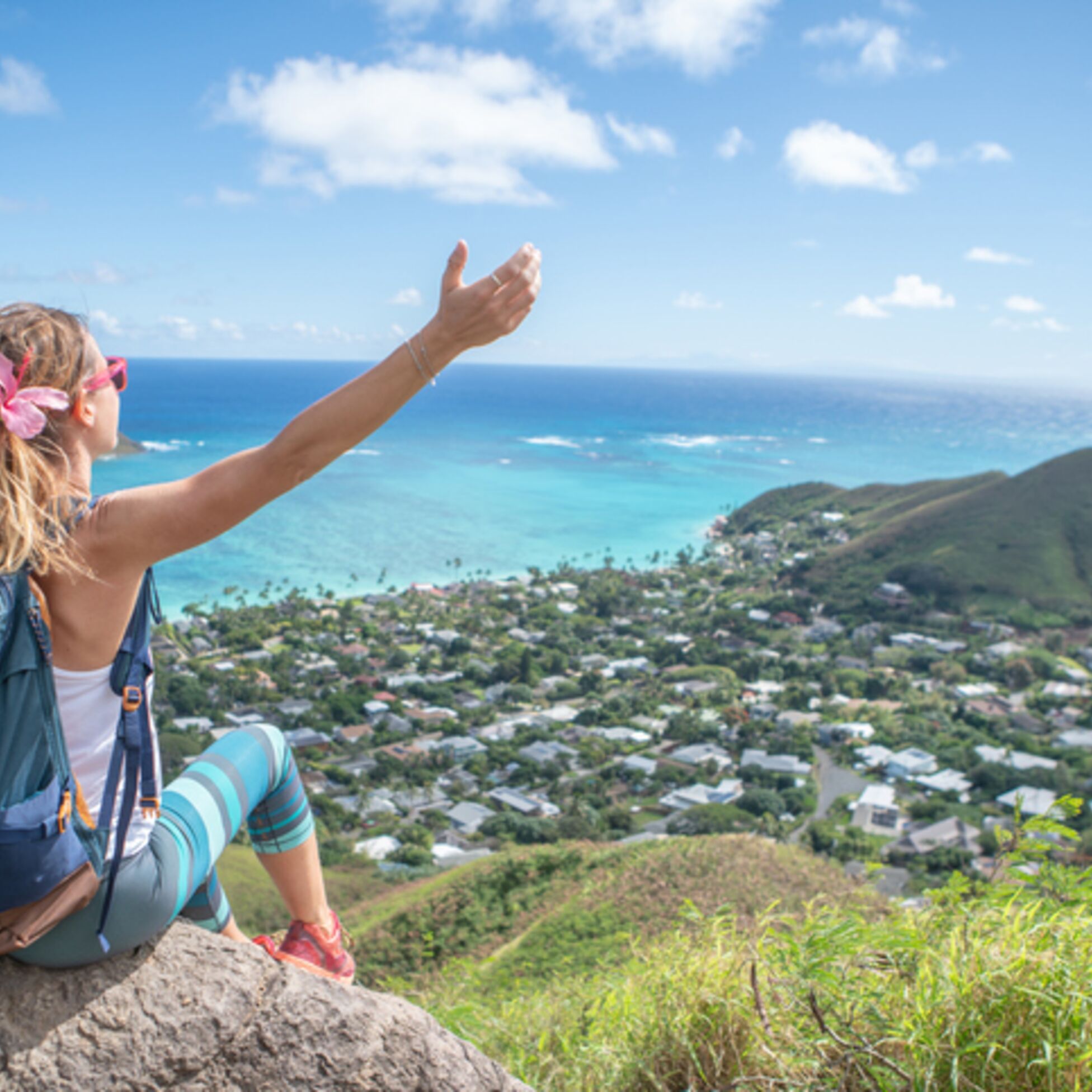 Junge Frau sitzt auf einem Hügel über Oahu und schaut aufs Meer
